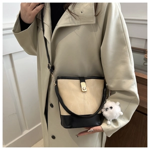 Detail view of beige bucket bag with black trim, metal lock and white plush pendant accessory