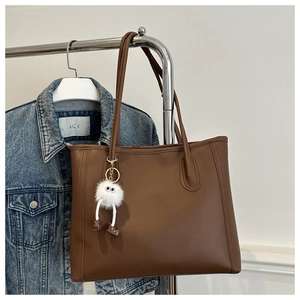 Detail of dark brown leather tote bag with a cute plush doll charm and fine stitching