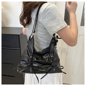 Detail of black tote bag with side pleats, decorative bow, and silver chain shoulder strap