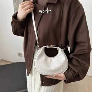White crescent moon shoulder bag with crocodile texture worn by a model in a brown coat