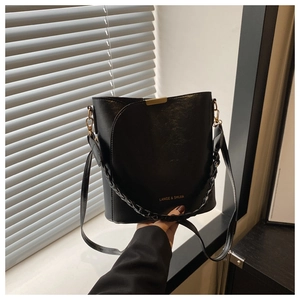 Detail of black bucket bag with gold hardware, leather texture and woven handle