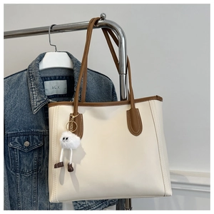Detail of a beige tote bag with brown trim and a funny plush monster charm on hanger