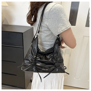 Detail of black pleated tote bag featuring side bows and metallic chain shoulder straps