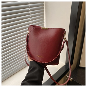 Detail of burgundy bucket bag with woven handle and gold brand logo text