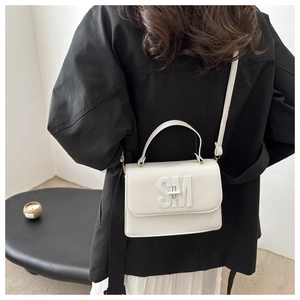Sac carré en cuir blanc à motif litchi avec lettres SM porté sur un manteau noir