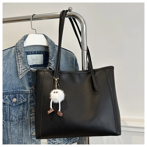 Detail of black PU leather tote bag with unique white fuzzy monster charm accessory