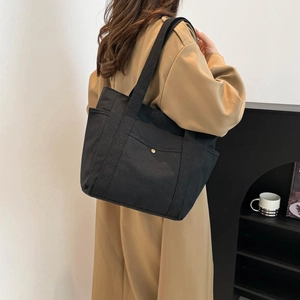 Minimalist black canvas tote bag with gold buckle and wide shoulder strap on a model