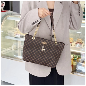 Detail of coffee brown tote bag with gold deer charm and chain strap on a model