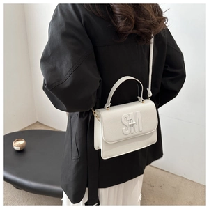 Détail du sac à bandoulière en cuir blanc avec logo SM embossé sur fond de manteau noir