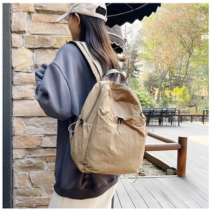 Side view of beige nylon backpack with drawstring pocket worn in outdoor park setting