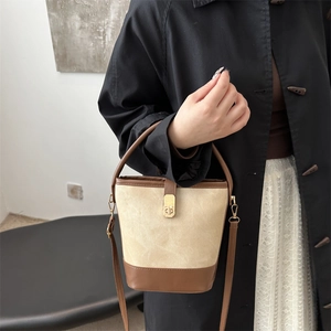 Beige bucket bag with brown leather trim and gold buckle worn by a model in a modern room