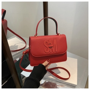 Détail du sac bandoulière en cuir rouge avec logo SM et fermoir pivotant en métal