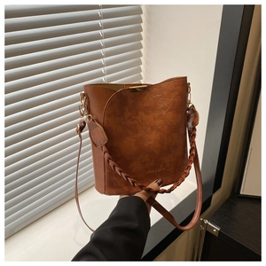 Macro detail of brown bucket bag featuring woven handle and gold brand logo texture