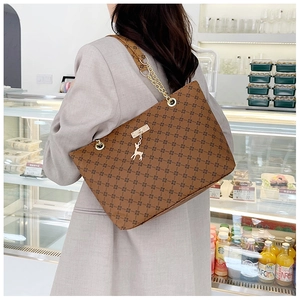 Detail of brown tote bag with geometric patterns, leather chain strap and golden deer charm
