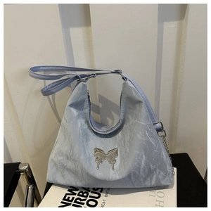 Détail du sac plissé bleu clair avec emblème papillon argenté et bandoulière en chaîne