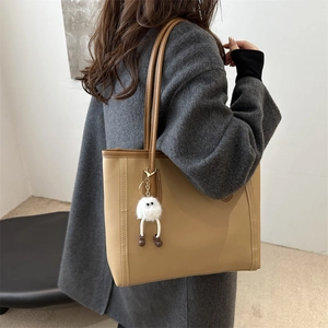 Fashionable khaki leather tote bag with long brown handles and a white plush charm