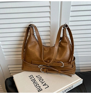 Detail of vintage brown PU leather tote with decorative silver buckles on white prop books