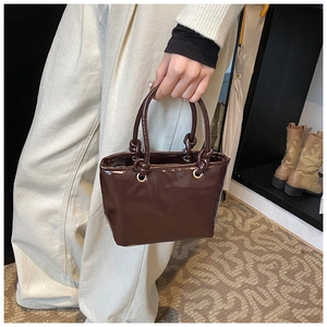 Détail d'un sac à main en cuir verni marron foncé avec poignée nouée et finition brillante