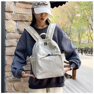 Outdoor look of a beige minimalist nylon backpack with drawstring side pockets and wide straps