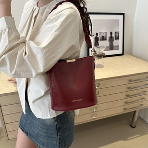 Minimalist burgundy leather bucket bag with woven strap and gold logo for daily commute
