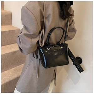 Détail d'un sac seau noir brillant avec anneaux métalliques et une fine bandoulière