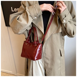 Modèle portant un sac seau bordeaux en cuir verni avec poignée nouée au style vintage