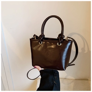 Détail du sac à main en cuir marron foncé brillant avec poignée ronde et anneaux dorés