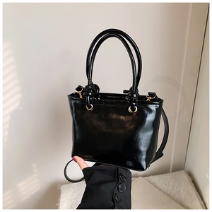 Détail du sac à main en cuir verni noir brillant avec garnitures dorées et poignées rondes