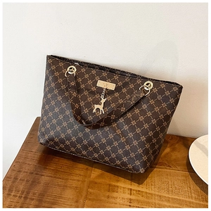 Detail of dark brown patterned tote bag with golden metal deer charm and luxury hardware