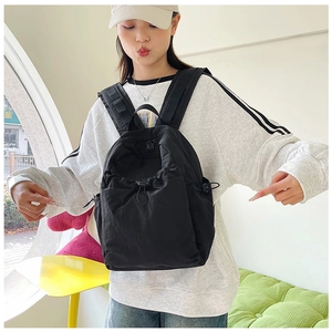 Close-up of a black nylon backpack on a model featuring drawstring closure and zipper pocket