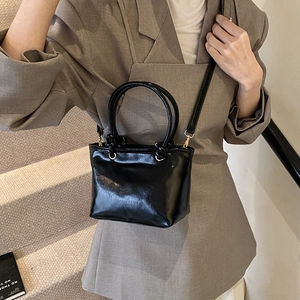 Sac seau minimaliste en cuir verni noir avec poignées et bandoulière réglable pratique