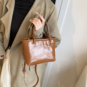 Sac seau marron brillant avec poignée nouée et détails dorés sur modèle