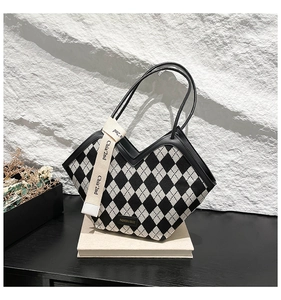 Detail of checkered tote bag with V-shaped opening, leather handles and decorative ribbon