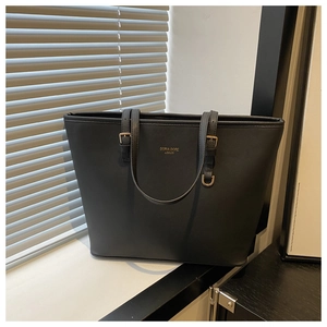 Detail of matte black tote bag showing gold logo and buckle on a sunlit window sill