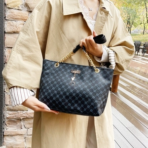 Elegant black tote bag with clover pattern and gold deer pendant on a trench coat model