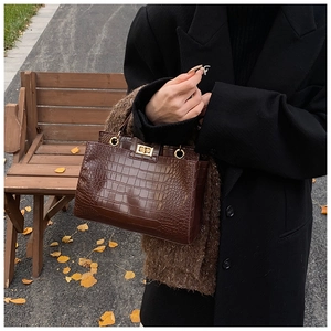 Detail of dark brown crocodile texture handbag with gold twist lock and plush charm