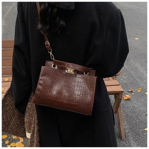 Detail of dark brown crocodile pattern handbag with glossy finish and metal turn-lock closure