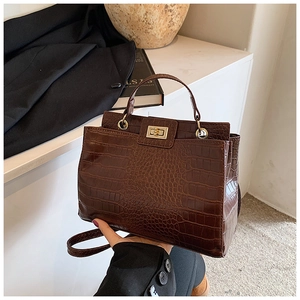 Close-up of dark brown crocodile embossed texture and golden twist lock on the handbag