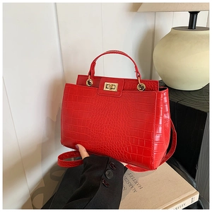 Detail of red crocodile texture handbag featuring a gold twist lock and metal handle ring