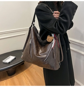 Detail of vintage brown PU leather tote bag featuring silver zippers and a plush bear charm