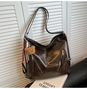 Detail of dark brown faux leather tote with dual diagonal zippers and a bear charm