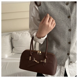 Detail einer dunkelbraunen Boston-Tasche aus Leder mit goldenen Elementen von einem Model gehalten