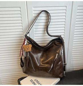 Close-up of deep brown oil wax leather tote bag with metal zippers and plush bear charm