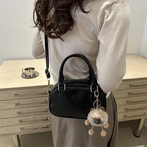 Retro black leather Boston handbag with brown plush bear charm in home setting