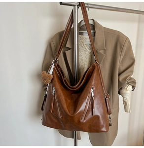 Detail of brown PU leather tote bag with vertical zippers and a cute plush bear charm