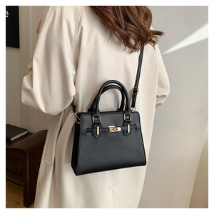 Detail of a black leather handbag with gold twist lock and adjustable shoulder strap