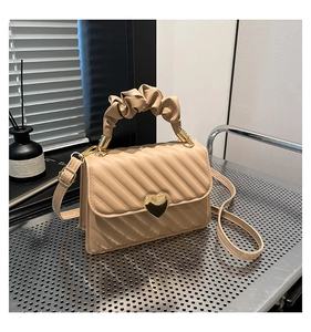 Dettaglio borsa trapuntata beige con chiusura a cuore dorata e manico a nuvola