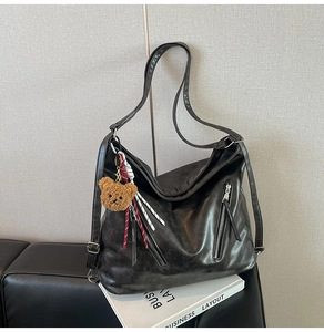 Detailed view of black faux leather tote bag with zip accents and plush bear charm