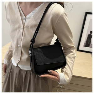 Close-up of black underarm bag featuring a woven textured flap and matte leather finish