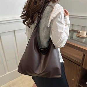 Minimalist dark brown leather tote bag with a soft drape, styled for urban commute fashion